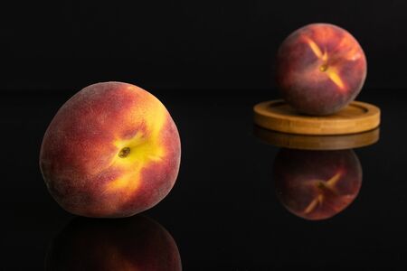 Group of two whole fresh red peach on a round bamboo coaster isolated on black glassの写真素材