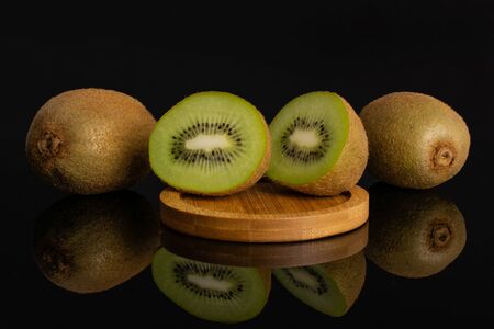 Group of two whole two halves of fresh green kiwifruit actinidia deliciosa on a round bamboo plate isolated on black glassの写真素材