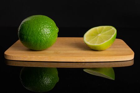 Group of one whole one half of fresh green lime on a bamboo cutting board isolated on black glassの写真素材