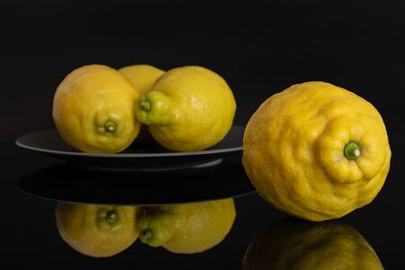 Group of four whole fresh yellow lemon one is in the front and the other three are in the back on a grey ceramic plate isolated on black glassの写真素材