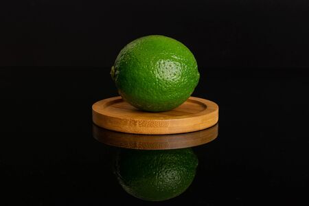 One whole fresh green lime on a round bamboo coaster isolated on black glassの写真素材