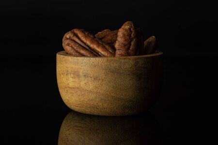 Lot of whole fresh brown pecan nut half in a wooden bowl isolated on black glass
