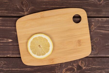 One slice of fresh yellow lemon on a bamboo cutting board flatlay on brown woodの写真素材