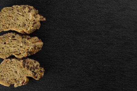 Group of three slices of fresh cereal baguette copyspace on right flatlay on grey dark stone