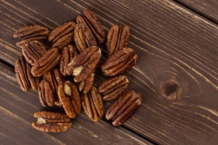 Lot of whole unshelled fresh brown pecan nut half flatlay on brown woodの写真素材