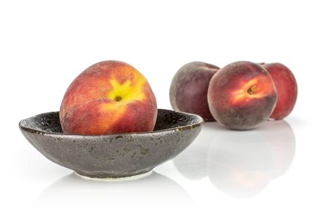 Group of four whole fresh red peach in a dark ceramic bowl isolated on white backgroundの写真素材
