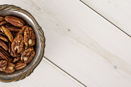Lot of whole fresh brown pecan nut half copyspace on right in old iron bowl flatlay on white wood
