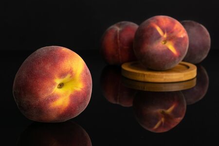 Group of four whole fresh red peach on a round bamboo coaster isolated on black glass