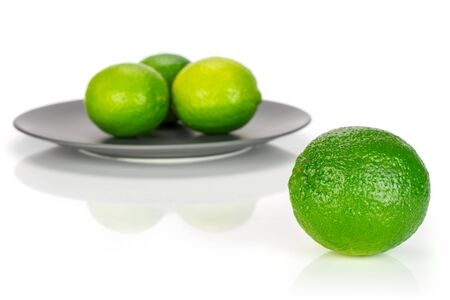 Group of four whole fresh green lime one is in the front and the rest is on a ceramic grey plate isolated on white backgroundの写真素材