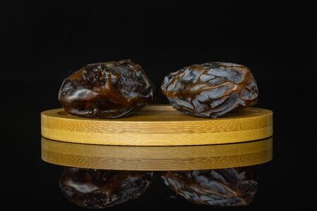 Group of two whole dried brown date medjool on bamboo plate isolated on black glass