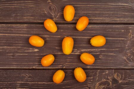 Lot of whole fresh orange kumquat arranged in a mandala flatlay on brown wood