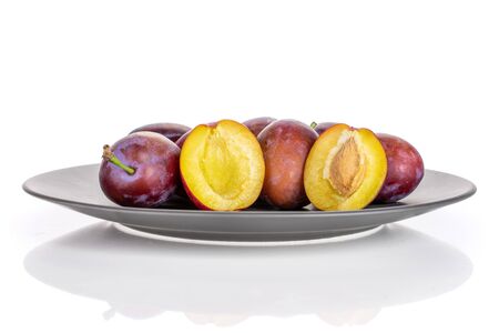 Group of lot of whole two halves of fresh blue plum with a stone on a gray ceramic plate isolated on white backgroundの写真素材