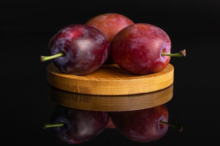 Group of three whole fresh blue plum on a round bamboo coaster isolated on black glassの写真素材