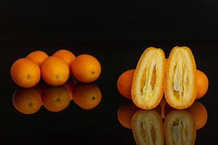 Group of lot of whole two halves of fresh orange kumquat isolated on black glassの写真素材