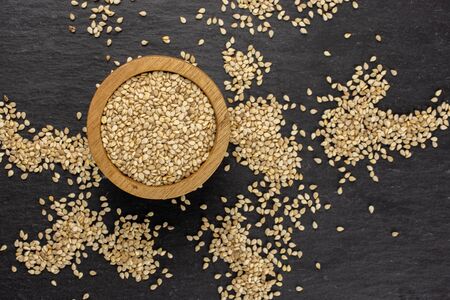 Lot of whole unpeeled sesame seeds in wooden bowl flatlay on grey stoneの写真素材