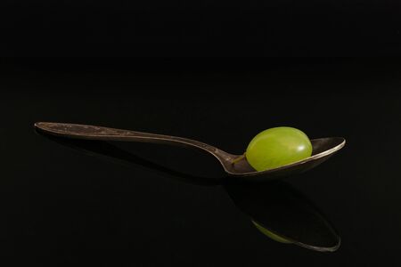 One whole fresh green grape with antique spoon isolated on black glassの写真素材