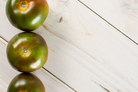 Group of three whole fresh greenish red tomato copyspace on right flatlay on white woodの写真素材