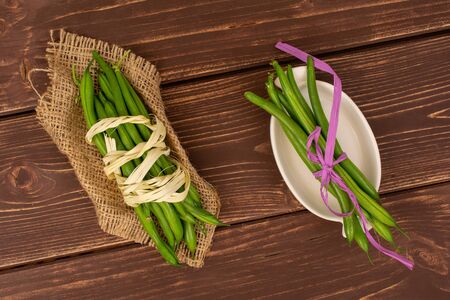 Lot of whole fresh green bean with natural bast , pink bast bow on natural sackcloth in white oval...
