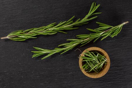 Group of two whole lot of pieces of fresh evergreen sprig of rosemary in a wooden bowl flatlay on grey stoneの写真素材