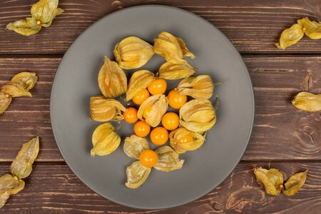 Lot of whole lot of pieces of fresh orange physalis on gray ceramic plate flatlay on brown woodの写真素材