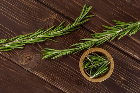 Group of two whole lot of pieces of fresh evergreen sprig of rosemary in a wooden bowl flatlay on brown woodの写真素材