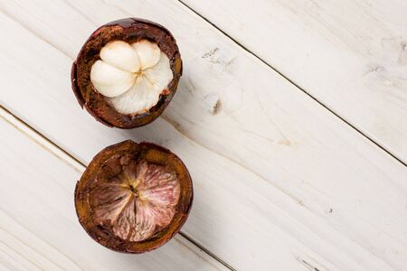 Group of two halves of deep purple mangosteen copyspace on right flatlay on white wood