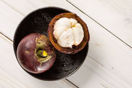 Group of one whole one half of deep purple mangosteen on grey ceramic plate flatlay on white woodの写真素材