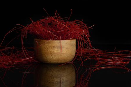 Lot of whole red chili pepper threads in wooden bowl isolated on black glass