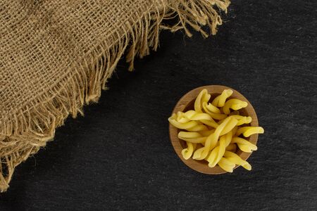 Lot of whole raw pasta gemelli in wooden bowl with jute cloth flatlay on grey stoneの写真素材