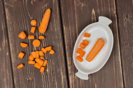 Group of two whole lot of pieces of stale orange stale baby carrot in a wooden bowl flatlay isolated on brown woodの写真素材