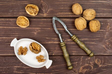 Group of lot of whole two pieces of ripe brown walnut in white oval ceramic bowl with old nutcracker flatlay on brown woodの写真素材