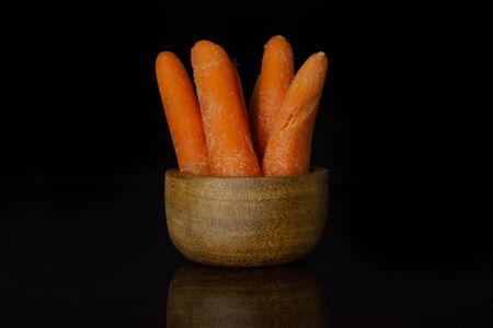 Group of four whole stale orange stale baby carrot in wooden cup isolated on black glassの写真素材