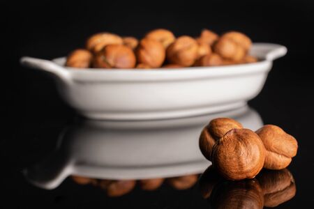 Lot of whole ripe brown hazelnut in white oval ceramic bowl isolated on black glassの写真素材
