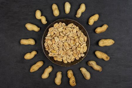 Lot of whole lot of halves of natural yellow peanut in dark ceramic bowl flatlay on grey stoneの写真素材