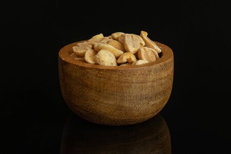 Lot of halves of natural yellow peanut in tiny wooden bowl isolated on black glassの写真素材