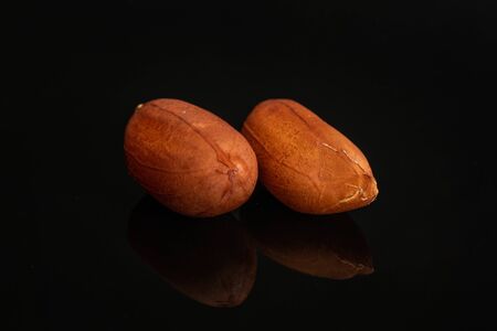 Group of two whole natural yellow peanut with skin in closeup isolated on black glass