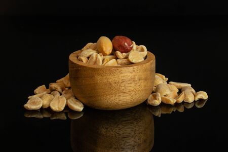 Group of two whole lot of halves of natural yellow peanut in tiny wooden bowl isolated on black glassの写真素材