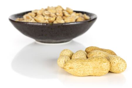 Lot of whole lot of halves of natural yellow peanut few is aside in dark ceramic bowl isolated on...