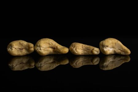 Group of four whole unsalted beige cashew isolated on black glassの写真素材