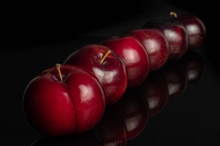 Group of six whole ripe red round plum placed diagonally in line isolated on black glassの写真素材