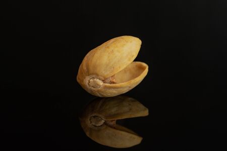 One piece of shell of ripe green pistachio in closeup isolated on black glass