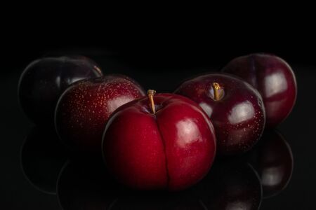 Group of five whole ripe red round plum one is in the front arranged symmetrically isolated on black glassの写真素材