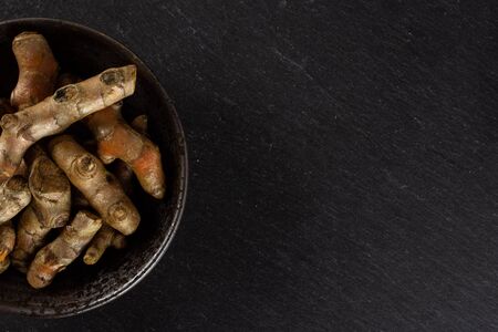 Lot of whole bright turmeric rhizome copyspace on right on grey ceramic plate flatlay on grey stone