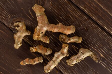 Lot of whole bright turmeric rhizome flatlay on brown wood