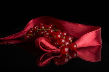 Lot of whole fresh red currant cluster with red ribbon isolated on black glassの写真素材