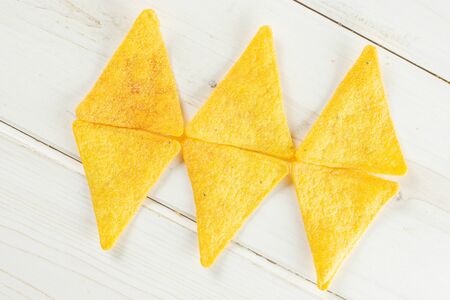 Group of six whole cheese tortilla chips three rhombs flatlay on white wood
