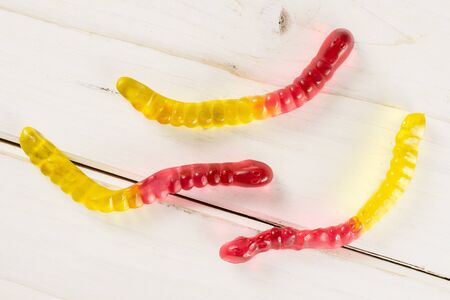 Group of three whole crimson yellow colourful jelly worm candy flatlay on white woodの写真素材
