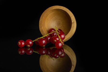 Lot of whole fresh red currant in bamboo bowl isolated on black glassの写真素材