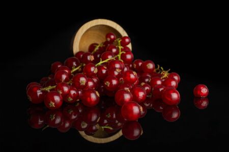 Lot of whole fresh red currant in bamboo bowl isolated on black glassの写真素材