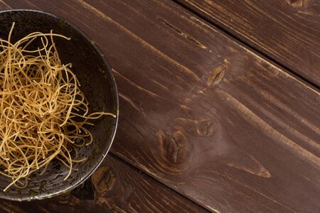 Lot of pieces of thin raw pasta noodles copyspace on right on grey ceramic plate flatlay on brown woodの写真素材